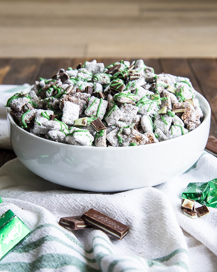 Mint Chocolate Muddy Buddies in a white bowl. They are drizzled with green candy melts over the top.