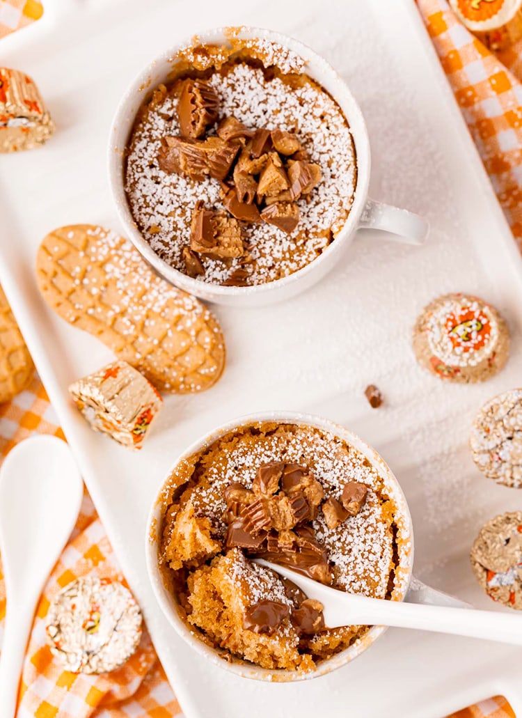 Two peanut butter nutter butter mug cakes on a white tray. They are topped with chopped peanut butter cups.