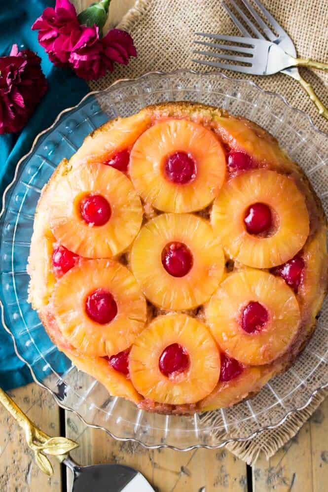 A pineapple upside down cake on a cake stand showing rings of pineapple with maraschino cherries in between them.