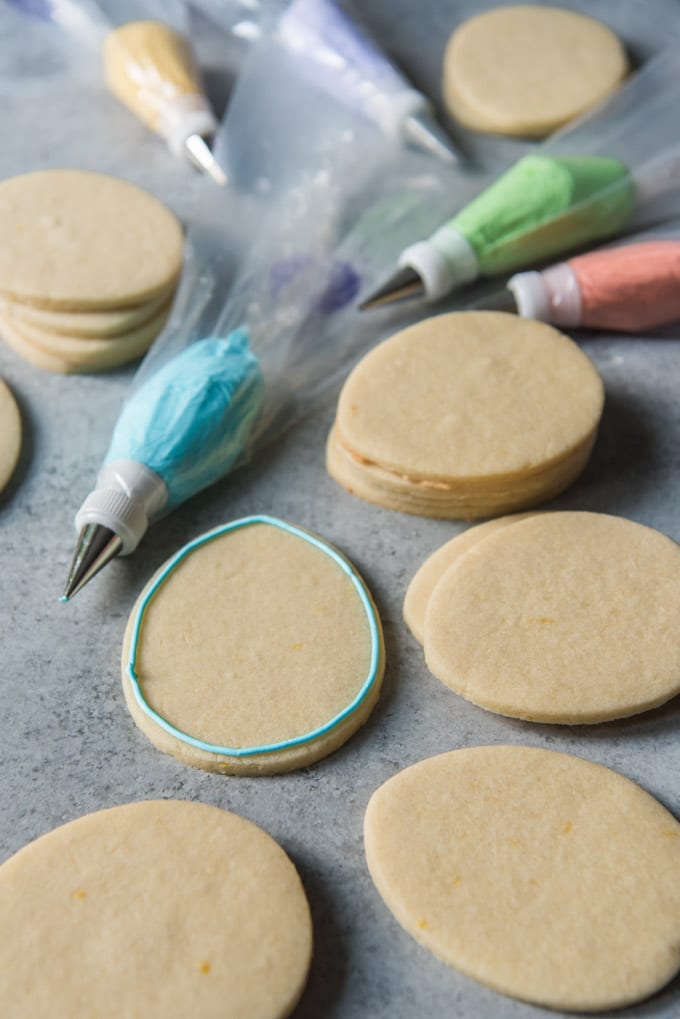 Sugar cookies shaped like Easter eggs, and one is decorated with a line of royal frosting on the outside.