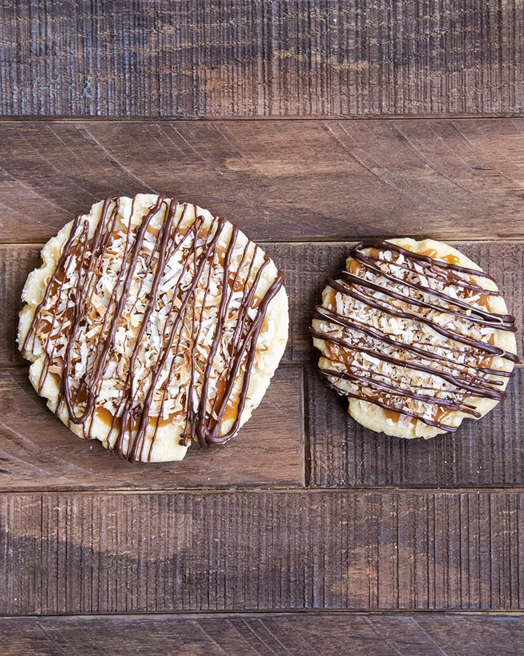 A big and a small sugar cookie each topped with caramel, toasted coconut, and drizzled with chocolate.