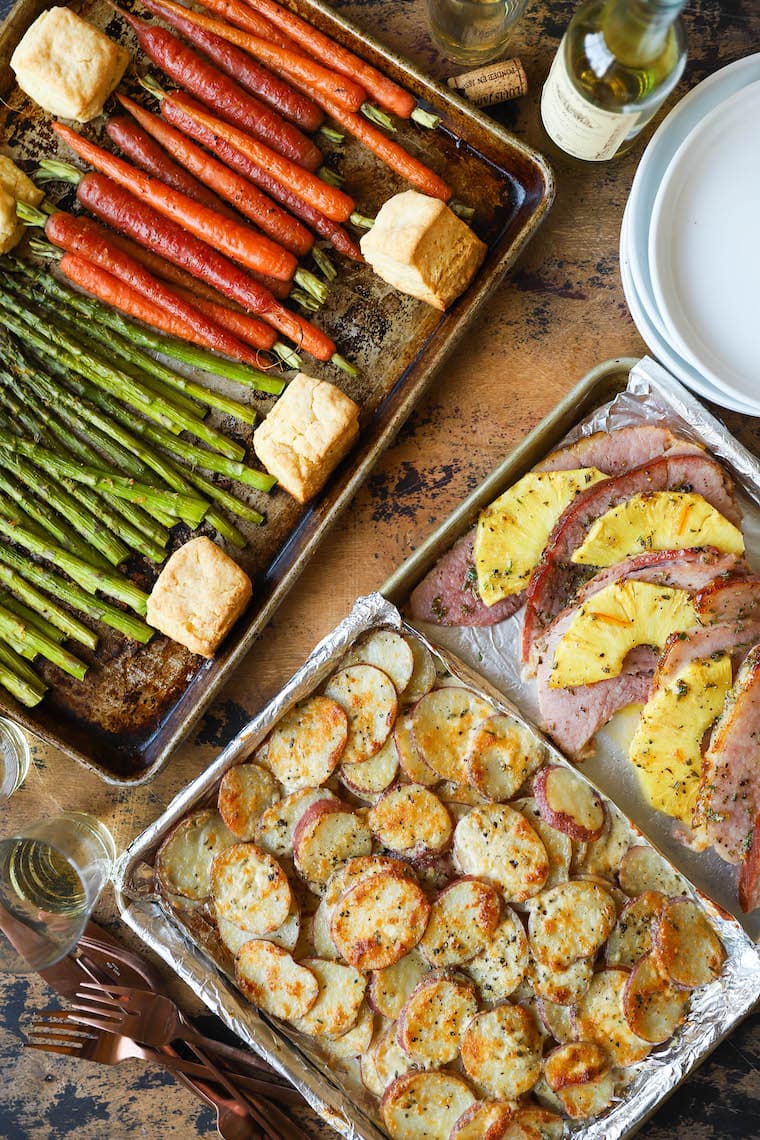 An overhead photo of two sheet pans of food with vegetables, pineapple ham, and scalloped potatoes.