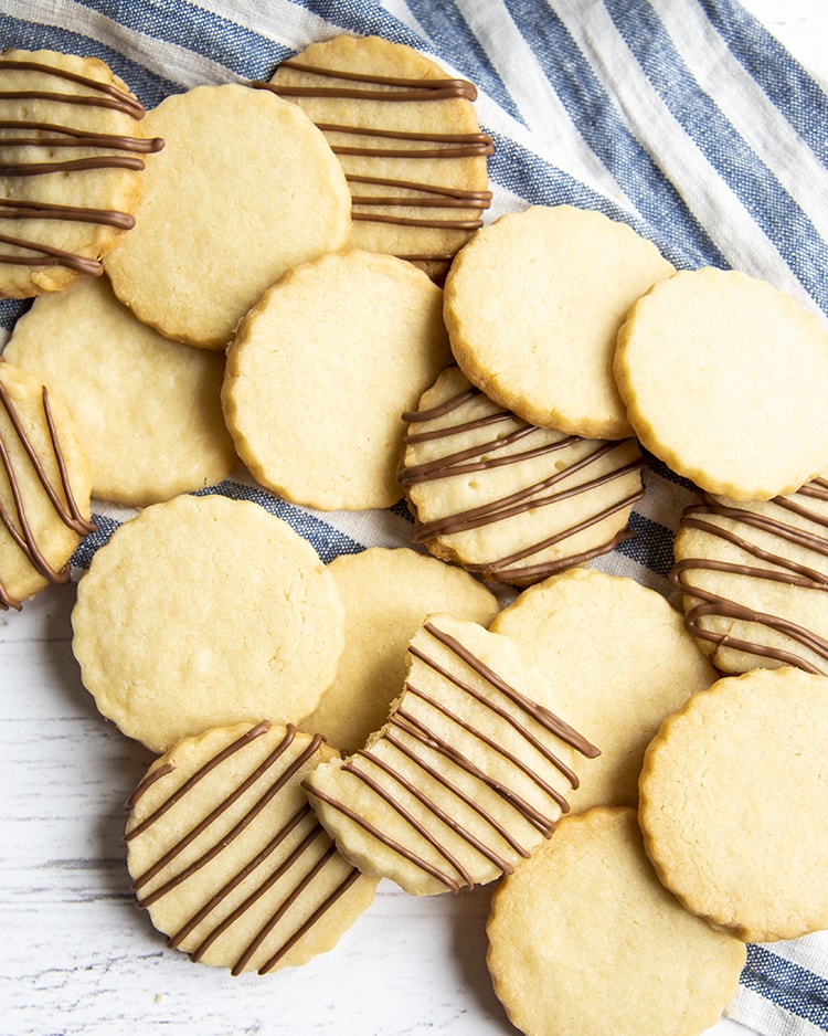 A pile of shortbread cookies, about half of them have chocolate drizzled thinly over the top.