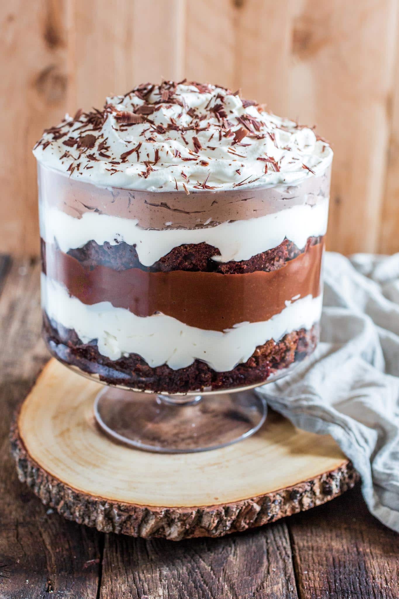 A trifle dish full of layeres of brownies, whipped cream, and chocolate pudding. The top is whipped cream sprinkled with chocolate shavings.