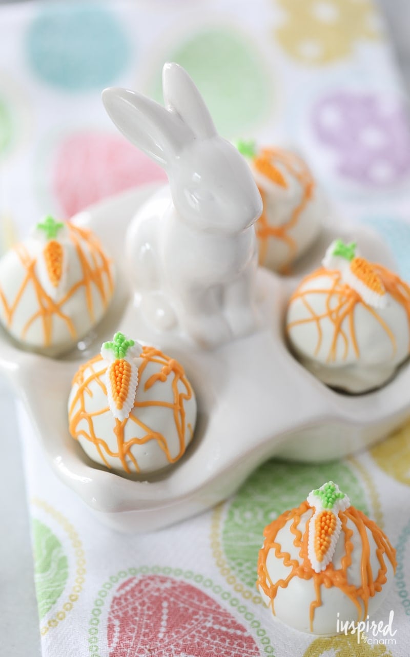 A bunny dish full of cake pops, drizzled with orange candy melts, and topped with a carrot shaped candy.