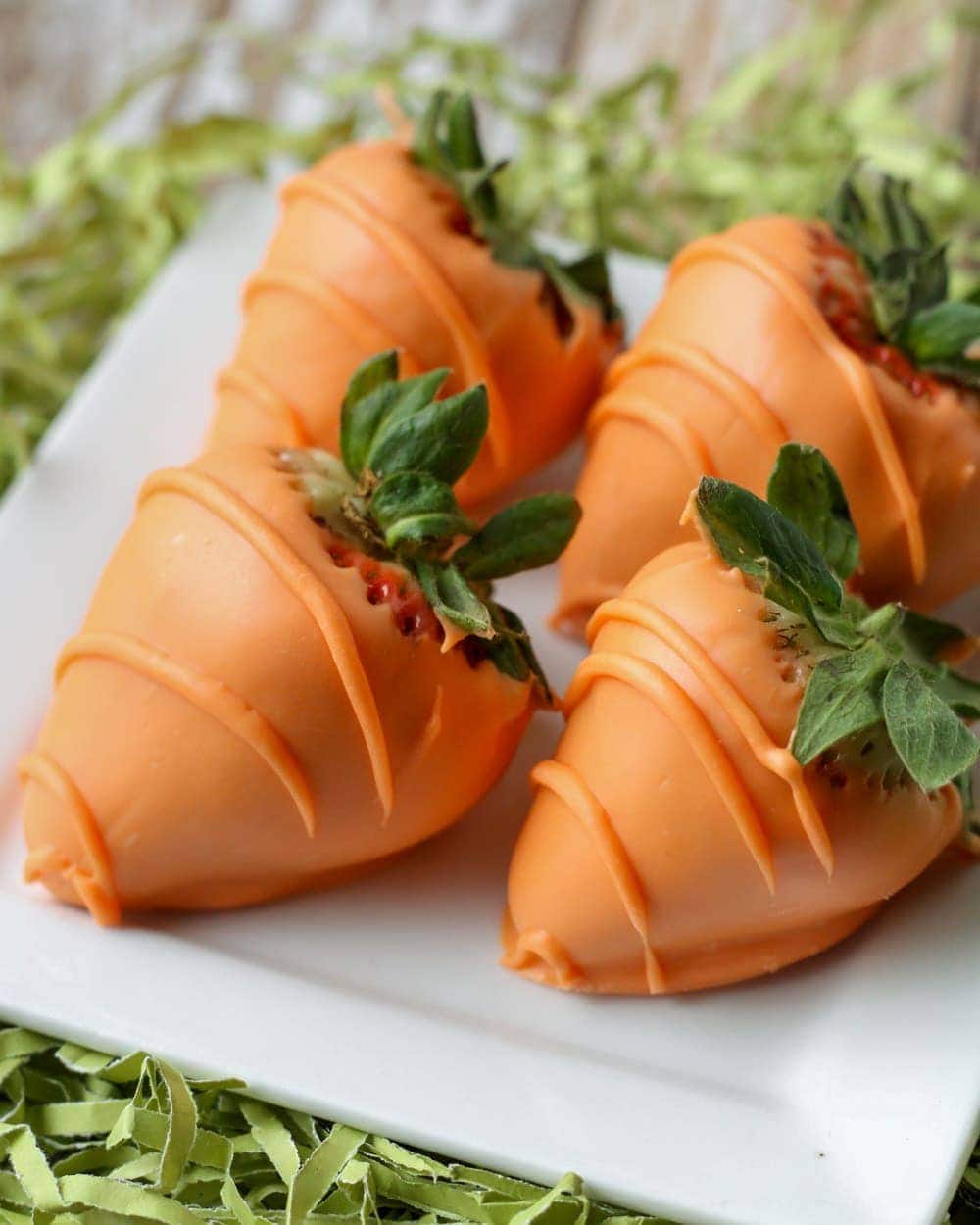 Strawberries dipped in orange candy melts and drizzled with more orange chocolate to look like carrots, all set on a plate.