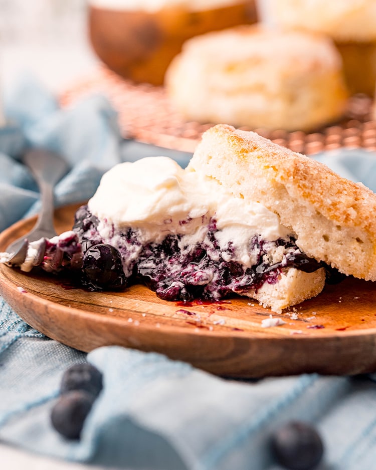 A blueberry shortcake on a wooden plate, with a bite taken out of it, and a fork next to it.