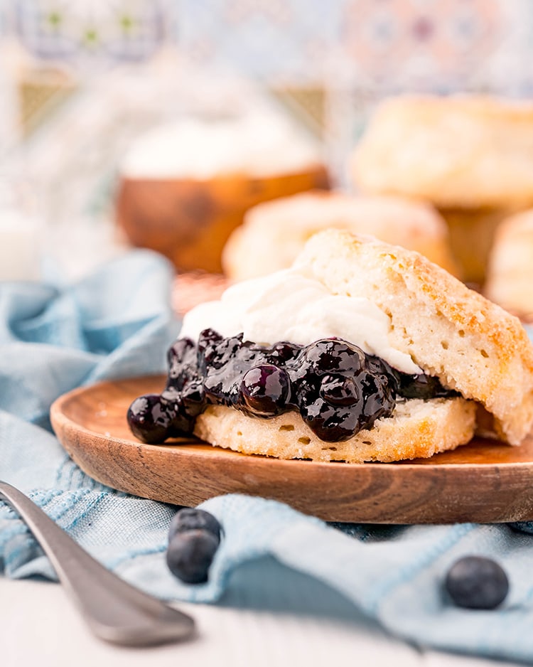 A biscuit shortcake with blueberry sauce and whipped cream in the middle on a wooden plate.