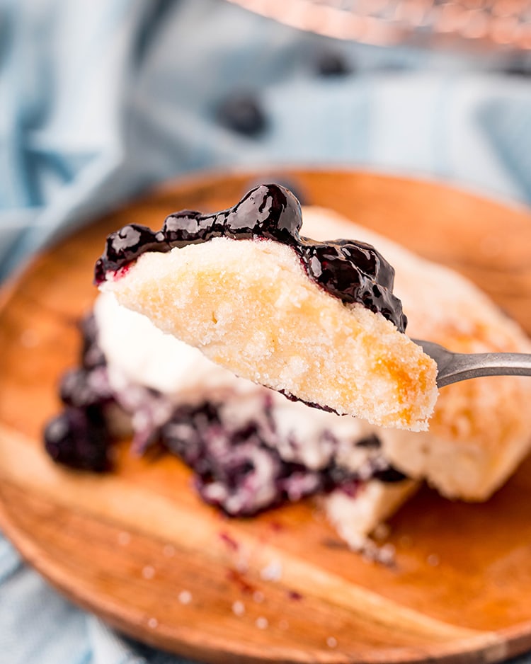 A fork holding a piece of a sugared biscuit, with blueberries on top.