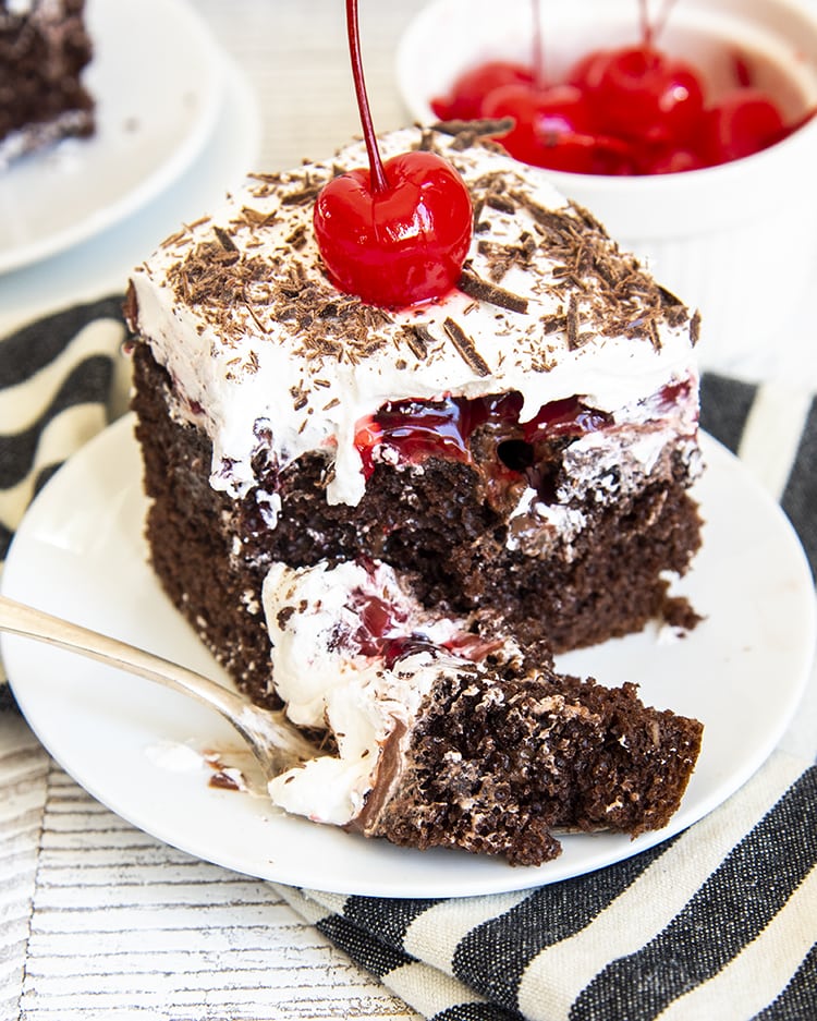 A piece of black forest poke cake with a forkful of cake in front of it.