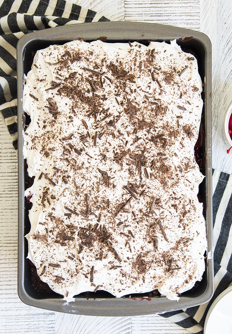 An overhead shot of a 9x13 pan of cake, you can see the whipped cream topped with chocolate shavings spread over the top.