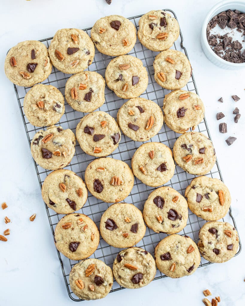 An above view of brown butter banana cookies full of walnuts, and chocolate chunks, on a wire cooling rack.