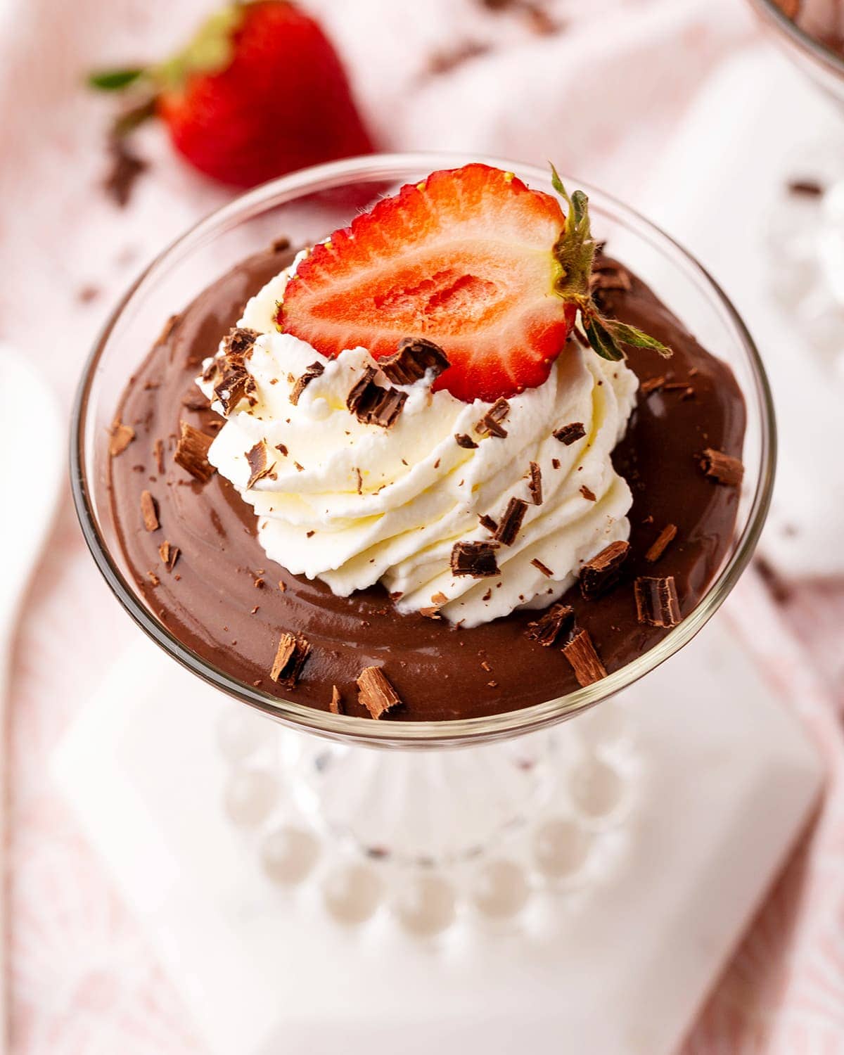 A glass jar full of chocolate pudding topped with whipped cream and half a strawberry.