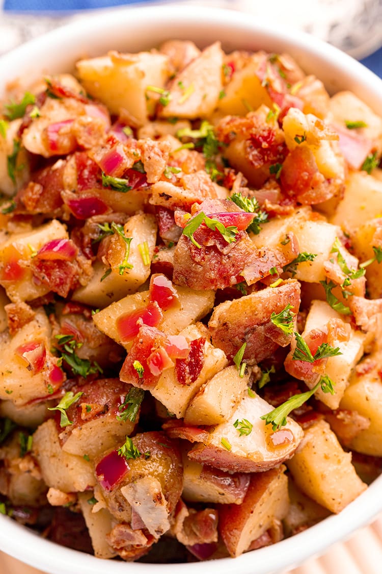 A close up of German potato salad with big pieces of red potatoes, bacon, red onion, and sprinkled with chopped parsley.