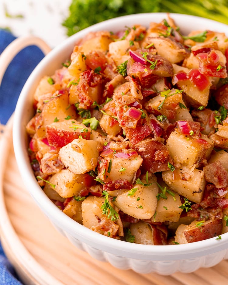 A white bowl full of german potato salad with big chunks of red potatoes, red onion, and bacon!