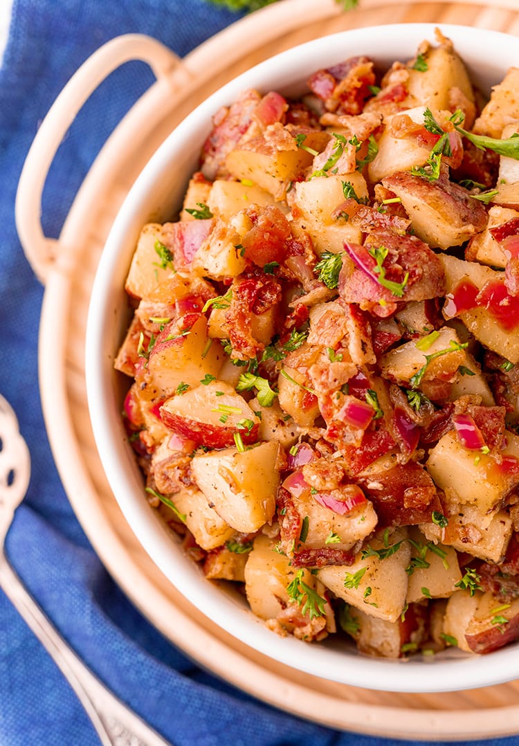 An overhead shot showing half of a bowl of red german potato salad. The salad also has red onion, and bacon, and is topped with chopped parsley.