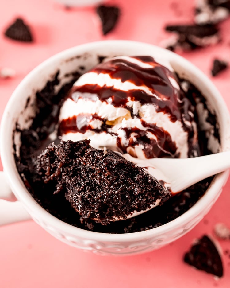 A spoon holding a bite out of a chocolate Oreo mug cake, it looks cakey, and a dark chocolate color.