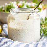 A clear jar full of homemade ranch dressing, about half full with a spoon also in the jar.
