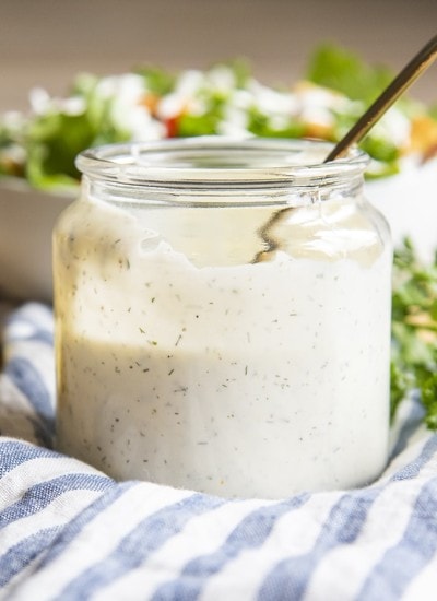 A clear jar full of homemade ranch dressing, about half full with a spoon also in the jar.