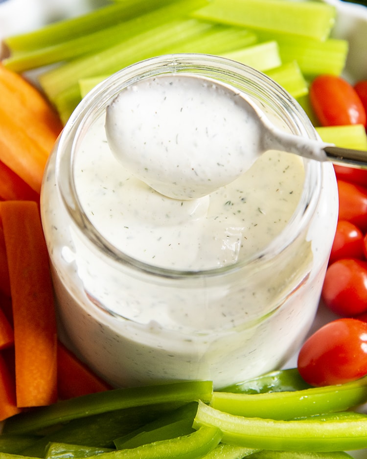 A spoonful of ranch dressing on a spoon above a glass bowl of the dressing.
