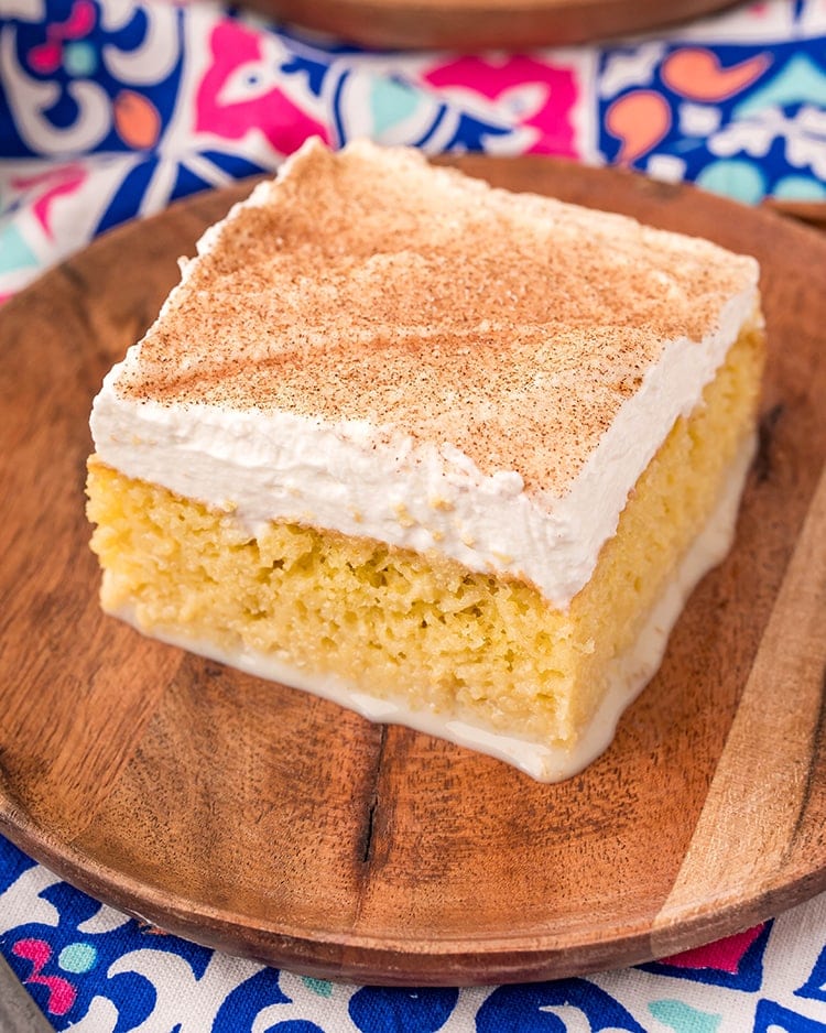 A piece of tres leches cake on a wooden plate.