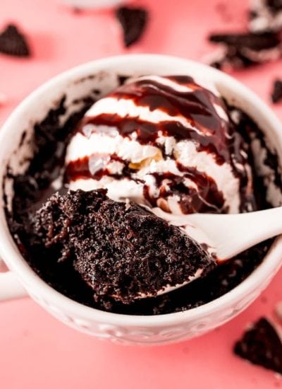 A spoon holding a bite out of a chocolate Oreo mug cake, it looks cakey, and a dark chocolate color.