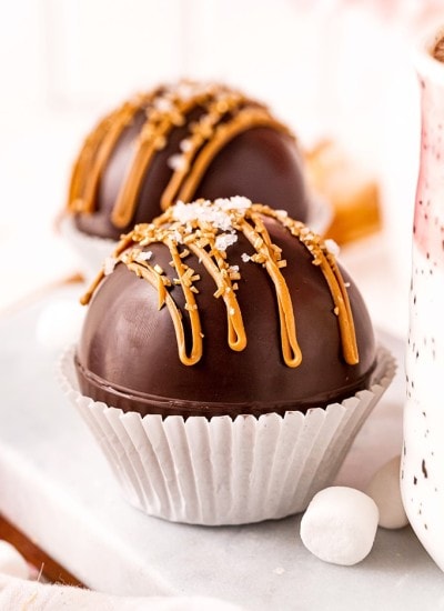 A hot chocolate bomb in a white paper muffin liner with caramel candy melts drizzled over the top, and sprinkled with sea salt.