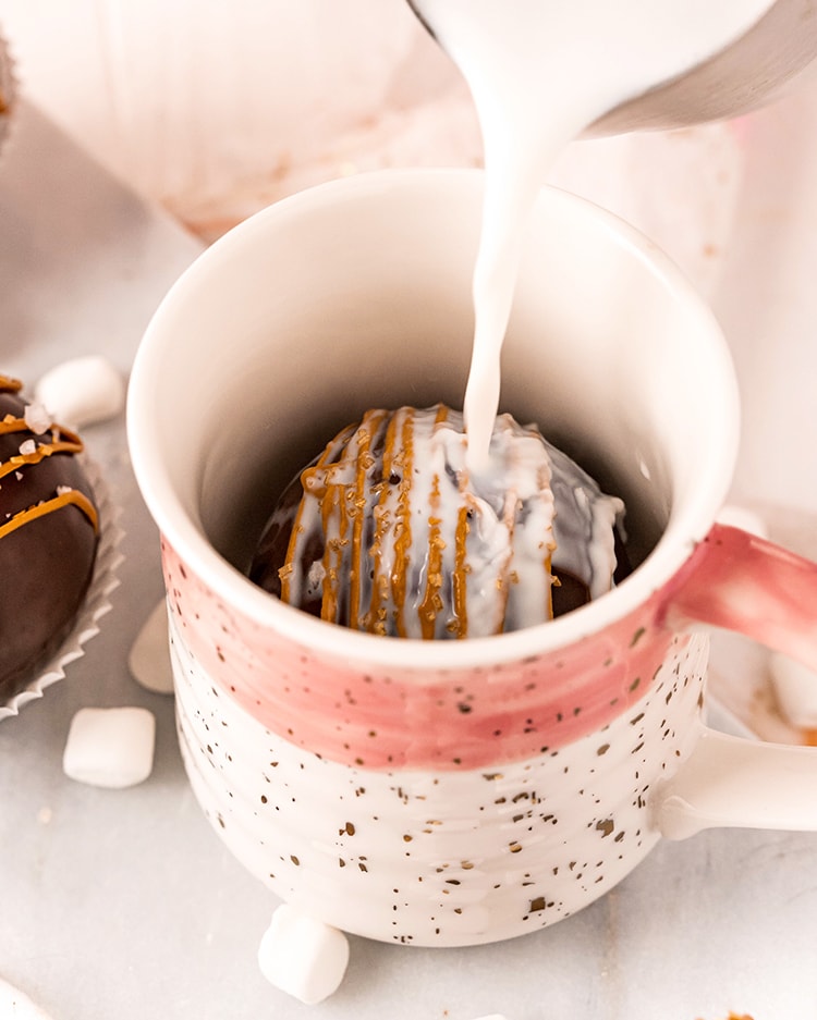 A hot chocolate bomb in the bottom of a mug with milk being poured over the top.