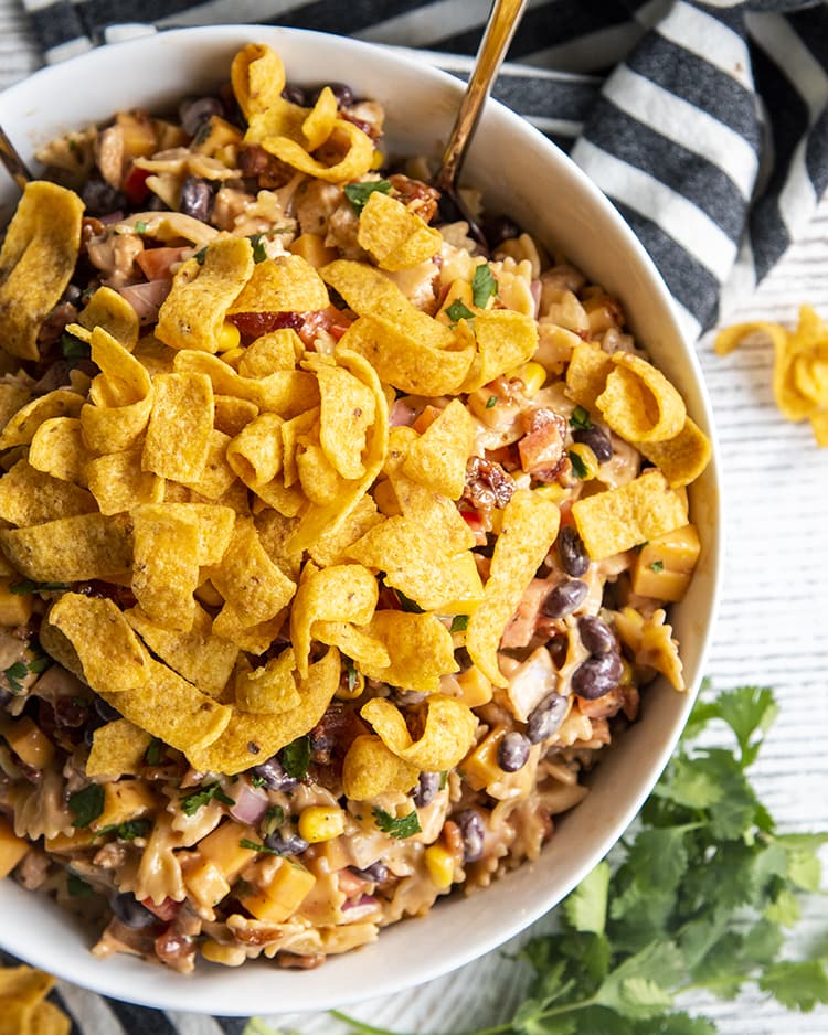 A bowl of BBQ chicken pasta salad, you can see mini farfalle, red onion, black beans, bell pepper, corn, and cilantro all in a creamy sauce. Topped with corn fritos!