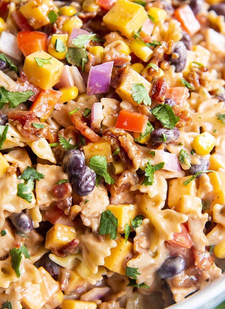 A close up of BBQ chicken pasta salad, you can see mini farfalle, red onion, black beans, bell pepper, corn, and cilantro all in a creamy sauce.