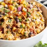 A bowl of BBQ chicken pasta salad, you can see mini farfalle, red onion, black beans, bell pepper, corn, and cilantro all in a creamy sauce.