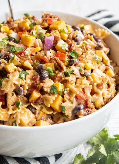 A bowl of BBQ chicken pasta salad, you can see mini farfalle, red onion, black beans, bell pepper, corn, and cilantro all in a creamy sauce.