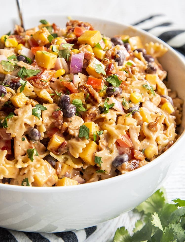 A bowl of BBQ chicken pasta salad, you can see mini farfalle, red onion, black beans, bell pepper, corn, and cilantro all in a creamy sauce.