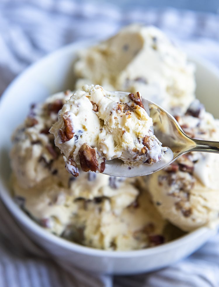 A spoonful of butter pecan ice cream above a bowl of ice cream.