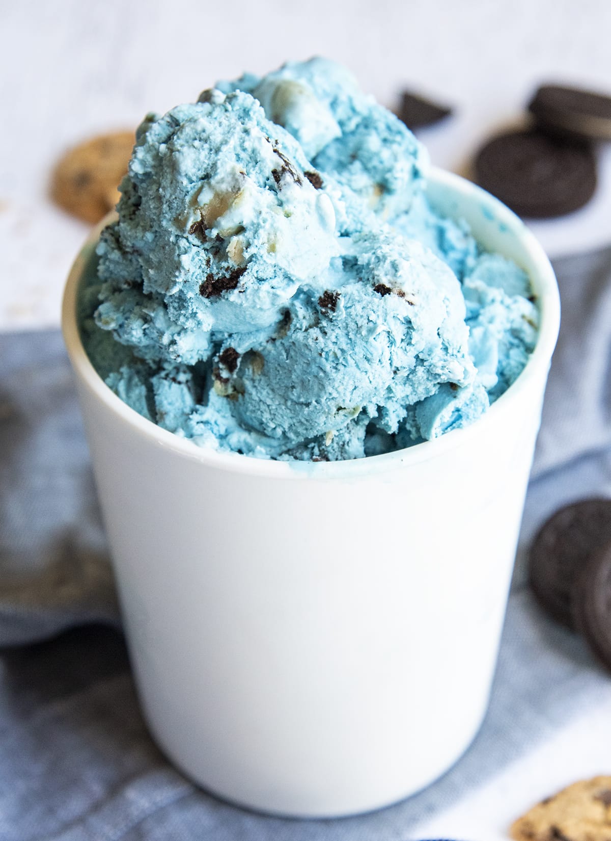 A white container of blue ice cream full of Oreo pieces and Cookie dough pieces.