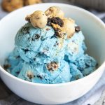 A bowl of blue ice cream full of oreos, and cookie dough pieces.