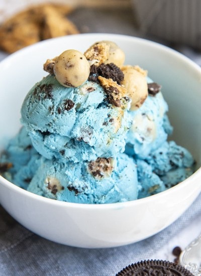 A bowl of blue ice cream full of oreos, and cookie dough pieces.