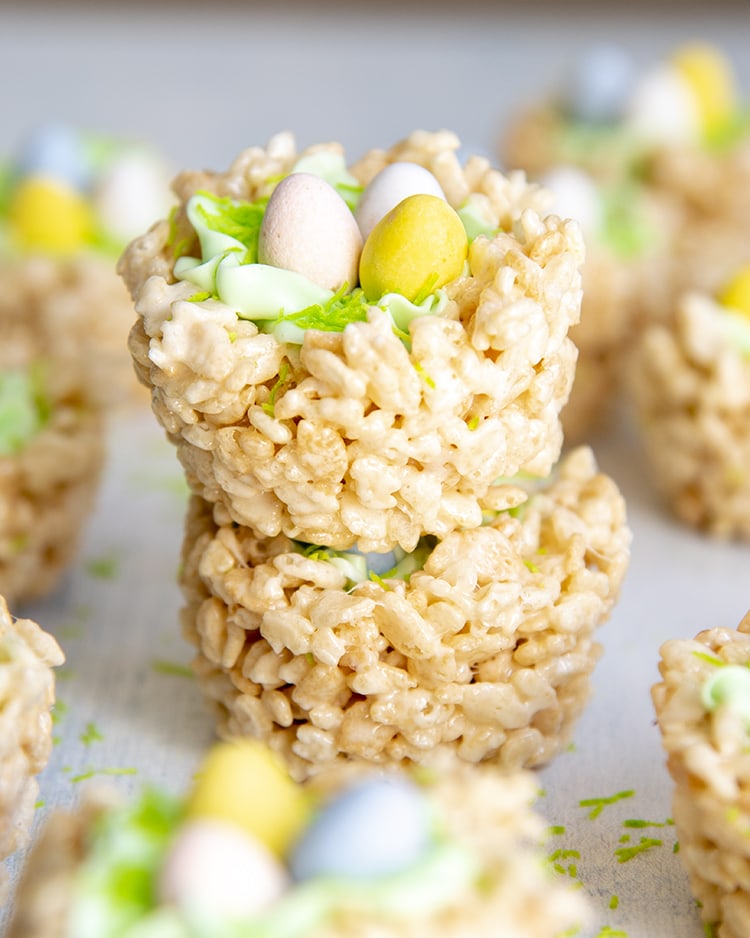 A stack of two rice krispie treat nests. The top shows the green frosting and three pastel colored cadbury eggs on top.
