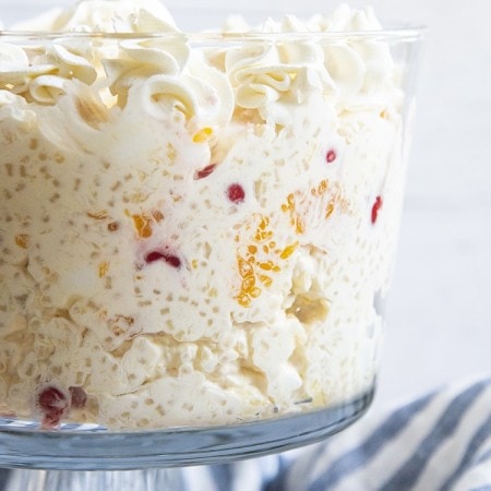 A trifle dish full of frog eye salad, topped with rosettes of whipped cream.