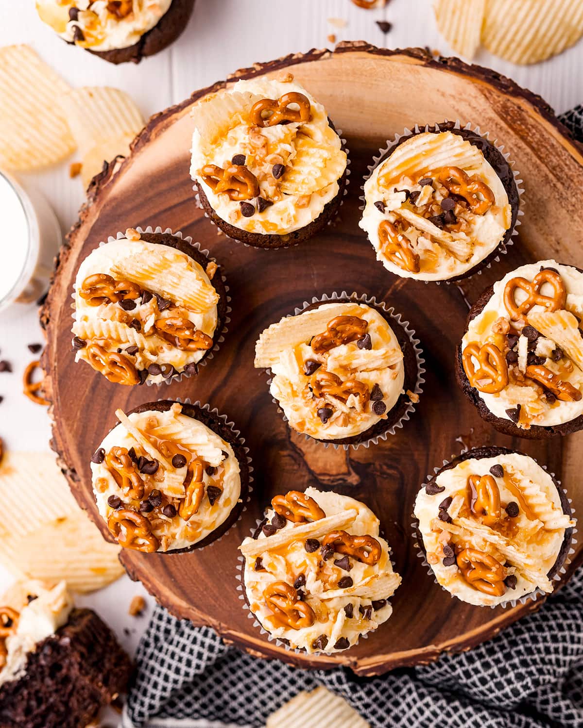 Chocolate cupcakes on a wooden stand topped with mini pretzels, ruffle chips, chocolate chips, and toffee pieces.