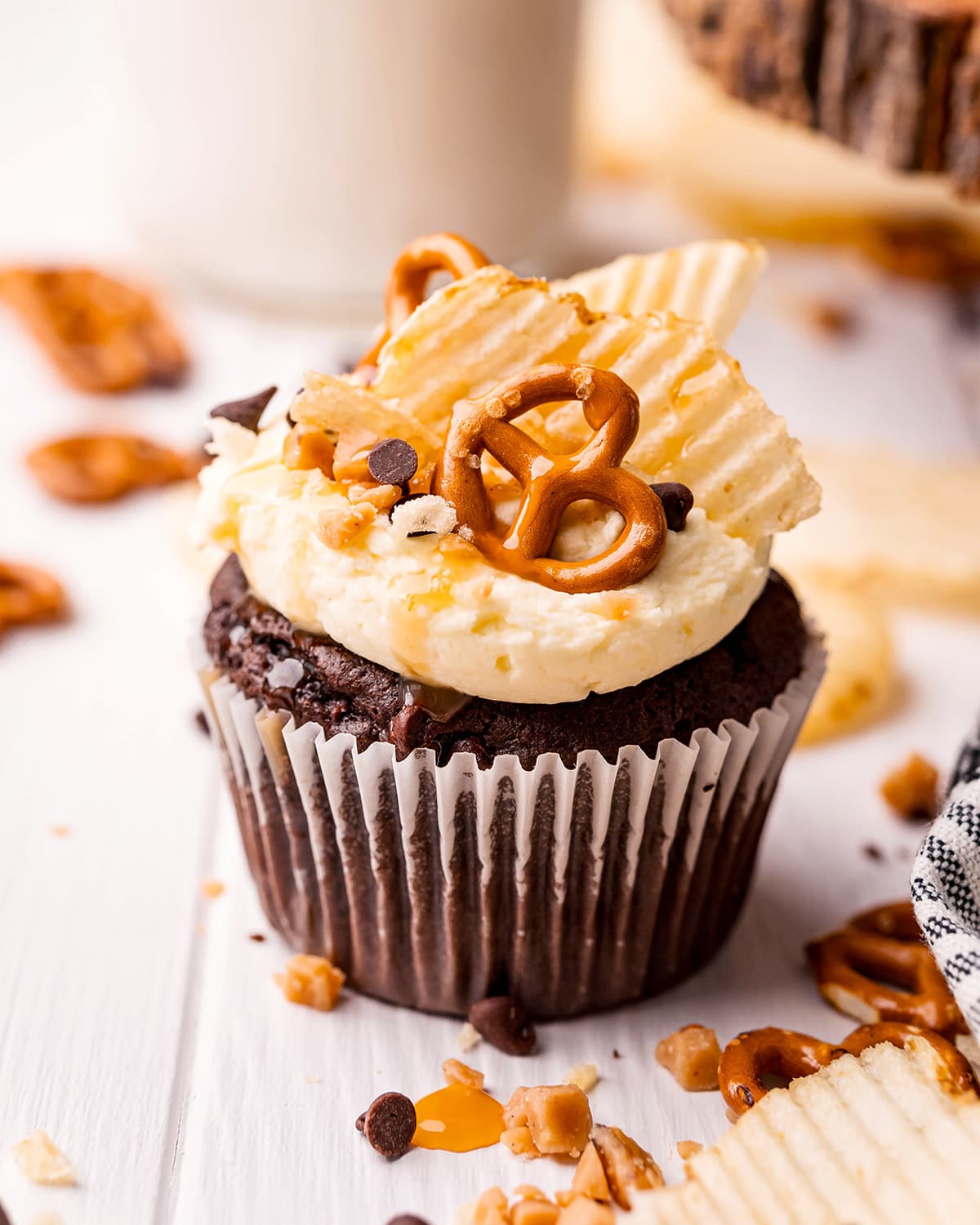 A chocolate cupcake topped with a white frosting, and chips, and caramel sauce.