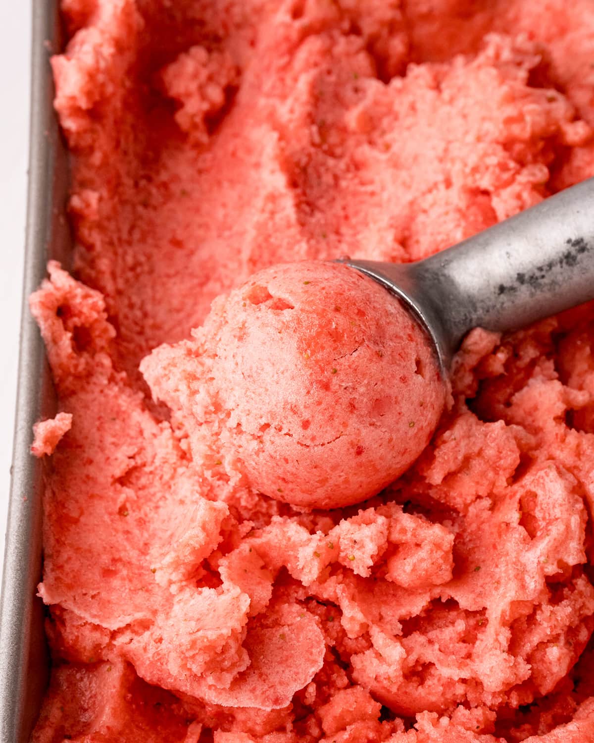 Strawberry pineapple sorbet in a pan, with a round scoop in an ice cream scooper.