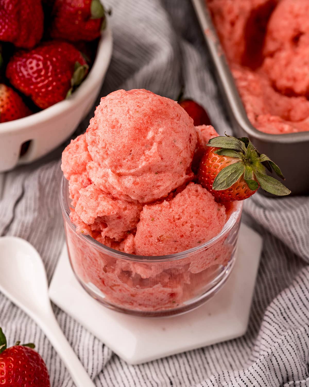 A clear glass bowl piled high with a pink strawberry sorbet, topped with a fresh strawberry.