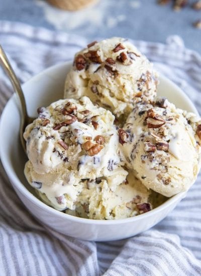 A bowl of 5 scoops of butter pecan ice cream, with lots of buttered pecans in each scoop, with a small spoon in the bowl.
