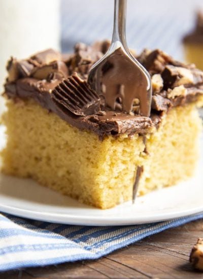 A piece of peanut butter cake with a cake mix topped with chocolate frosting and peanut butter cups. With a fork in the cake cutting out a bite.