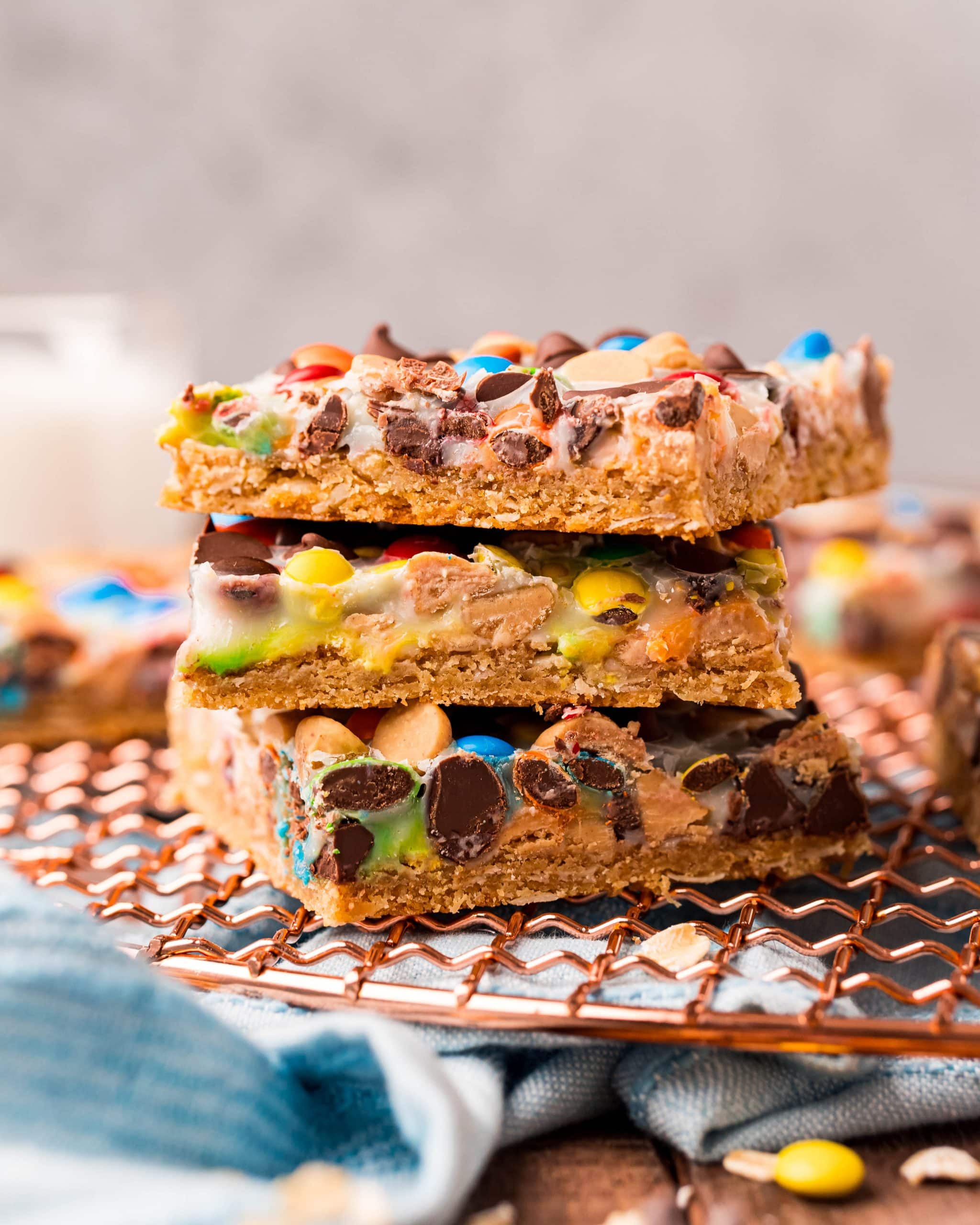 A stack of magic bars with m&ms and chocolate chips showing through the white sweetened condensed milk on top.