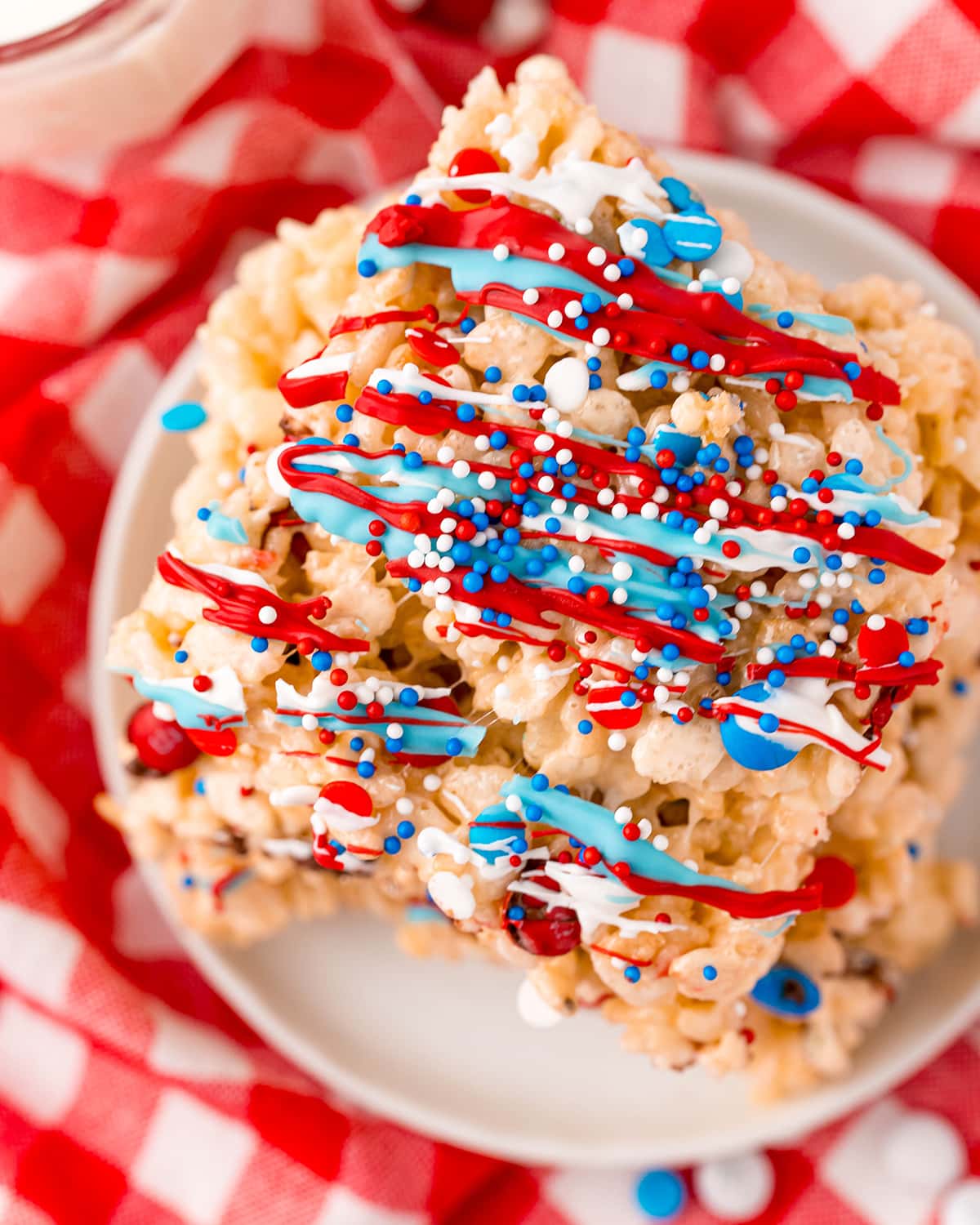 A 4th of July Rice Krispie treat on a plate, drizzled with red, white, and blue candy melts, and covered in sprinkles.