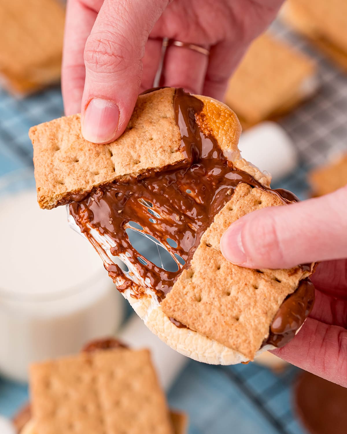 A hand holding a s'more, broken in half showing the gooey marshmallow and chocolate separating in the middle.