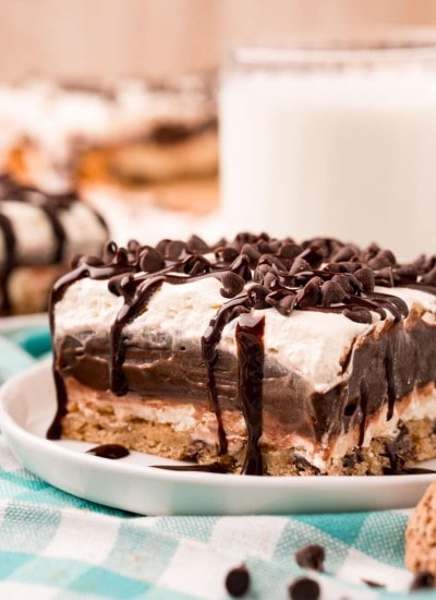 A piece of layered chocolate hip cookie delight on a small plate, topped with mini chocolate chips, and drizzled with chocolate syrup.