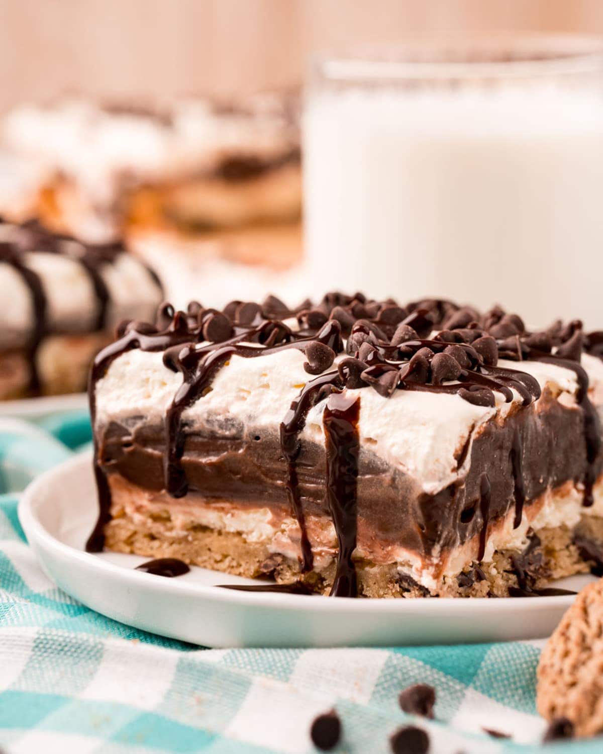 A piece of layered chocolate hip cookie delight on a small plate, topped with mini chocolate chips, and drizzled with chocolate syrup.